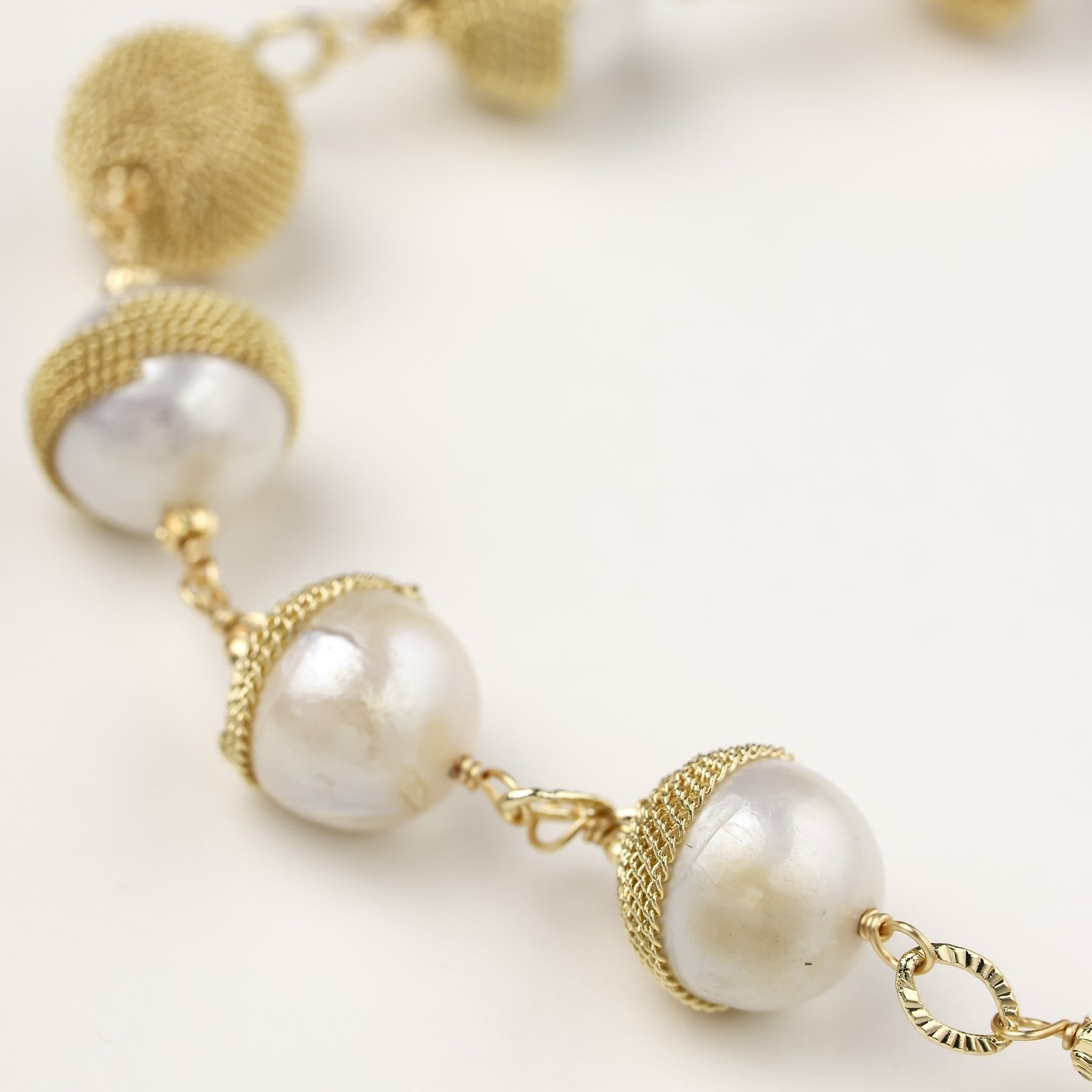 Adjustable bracelet featuring baroque pearls wrapped in gold mesh wire with delicate chain links on cream background.
