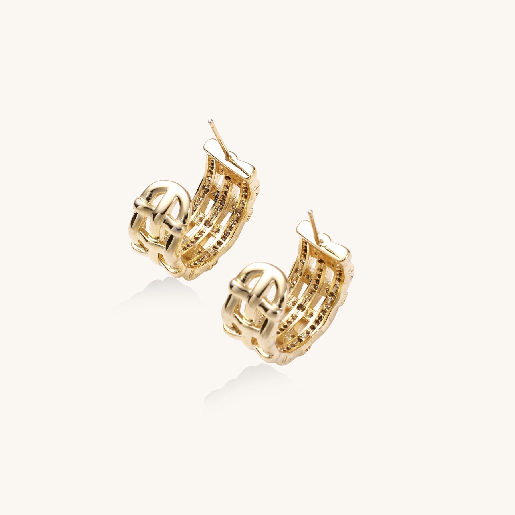 Close-up of geometric gold-plated hoop earrings with crystal pave in intricate lattice pattern on neutral background.