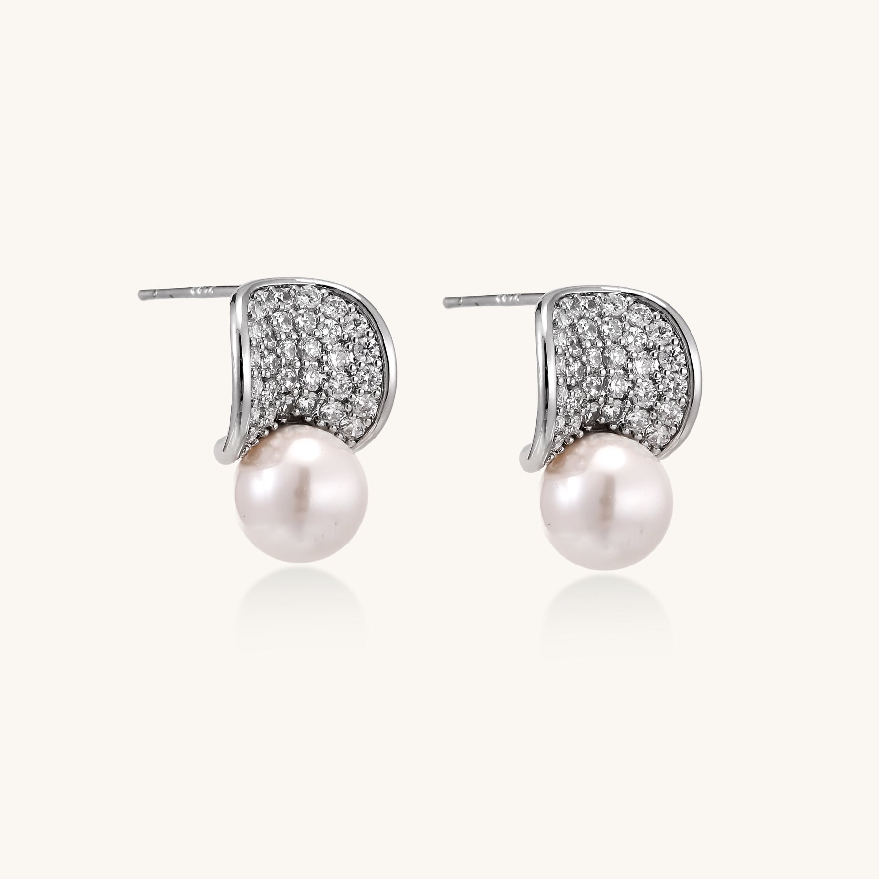 Elegant gold-plated curved earrings with diamond pavé crescents and suspended freshwater pearls on neutral background.