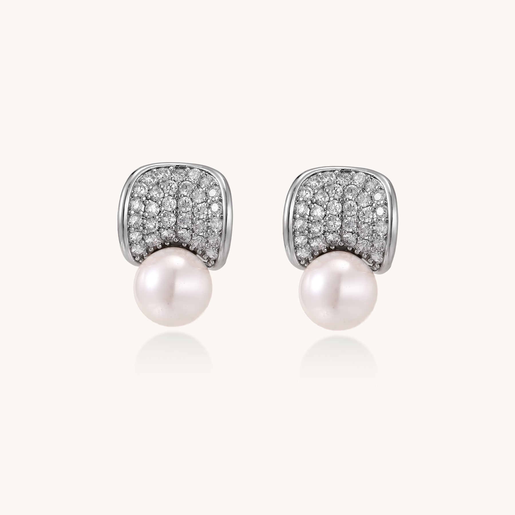 Elegant gold-plated curved earrings with diamond pavé crescents and suspended freshwater pearls on neutral background.
