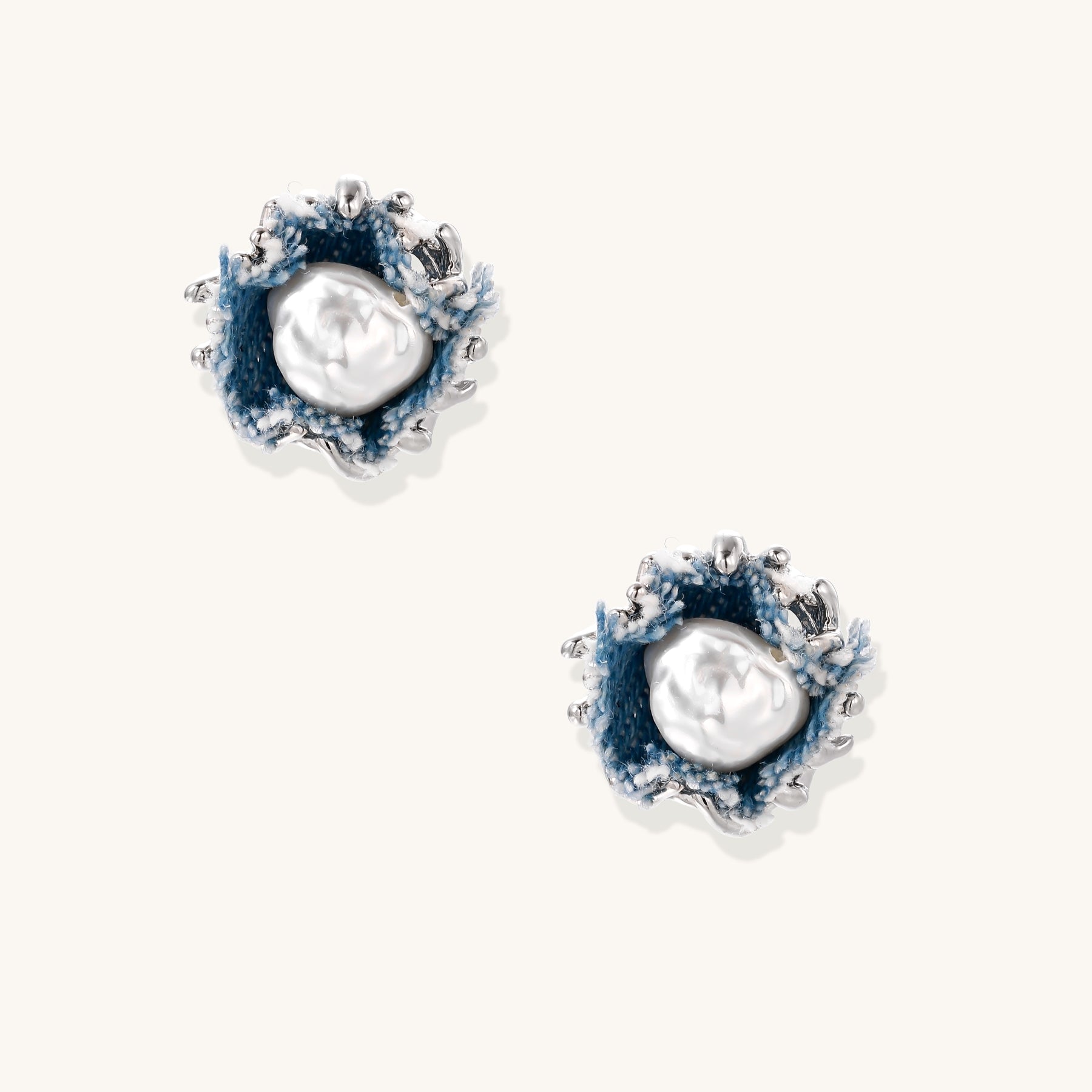 Circular stud earrings with white pearl centers, blue denim fabric, and gold-silver metallic edges on white background.