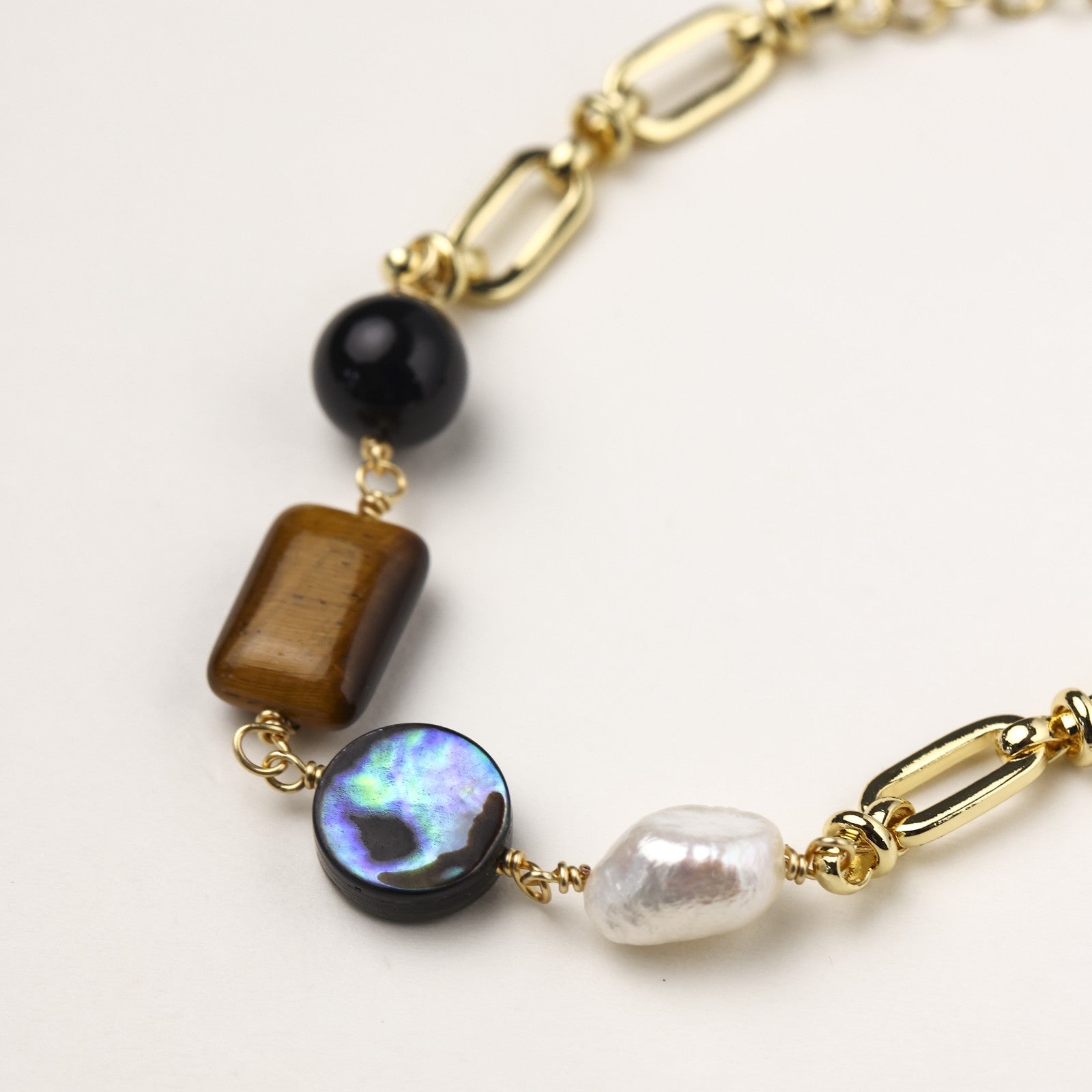 Gold-plated chain bracelet featuring tiger's eye, obsidian, freshwater pearls and abalone shell on white background