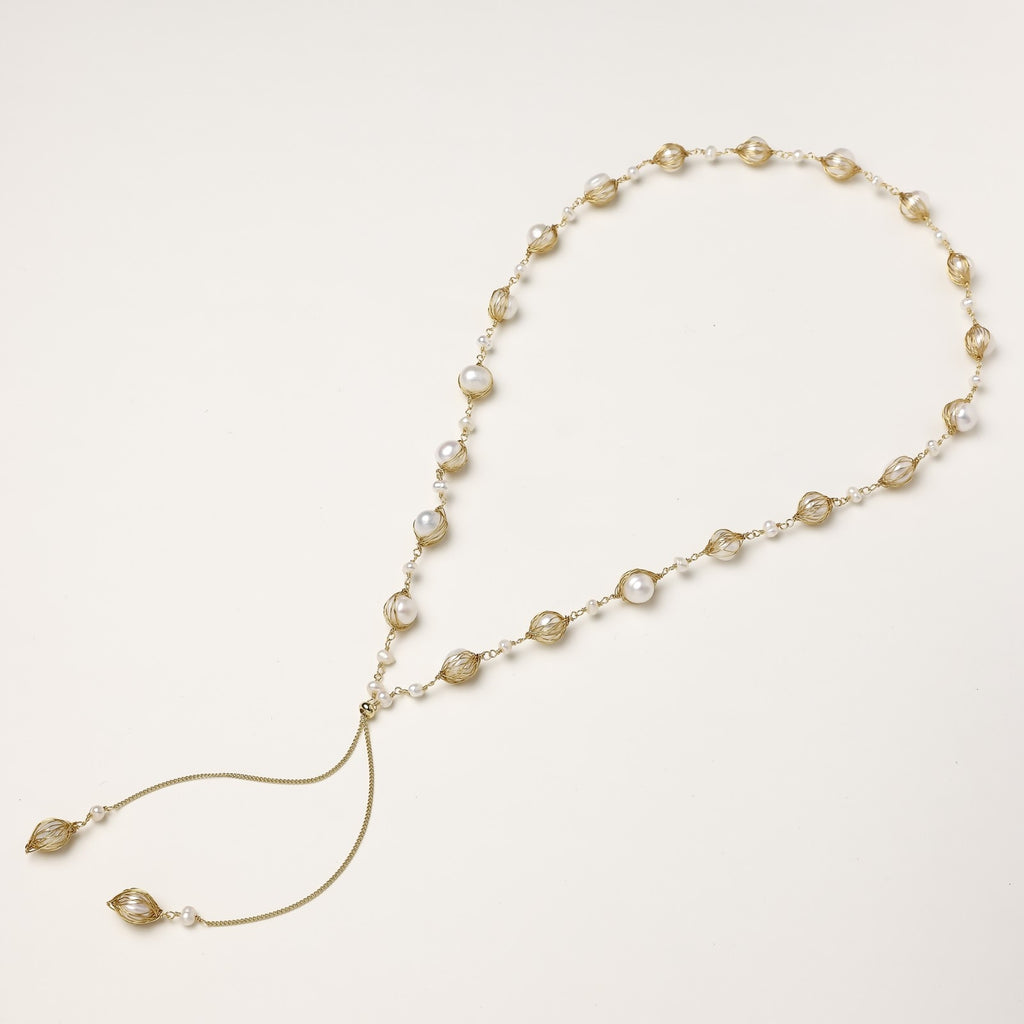 Long gold-plated lariat necklace with wire-wrapped freshwater pearls and chain tassel detail on cream background.