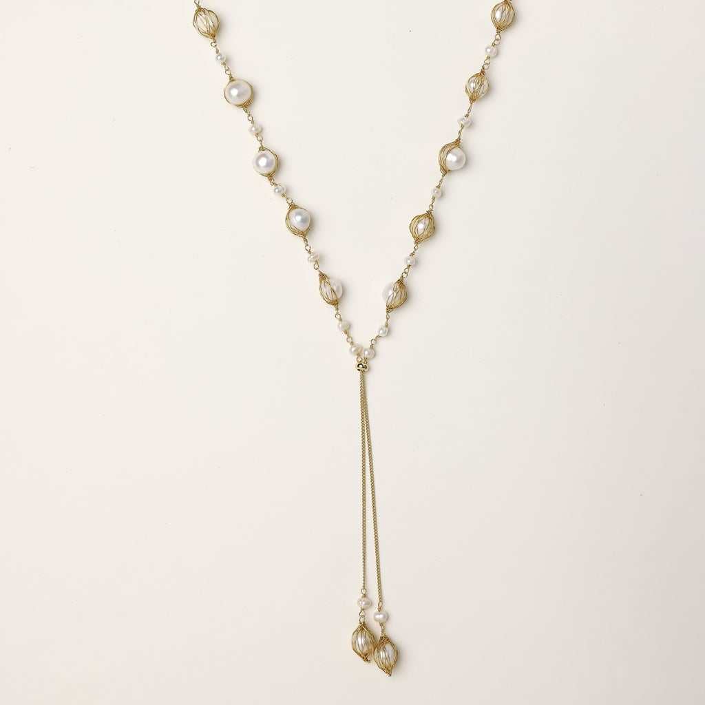 Long gold-plated lariat necklace with wire-wrapped freshwater pearls and chain tassel detail on cream background.