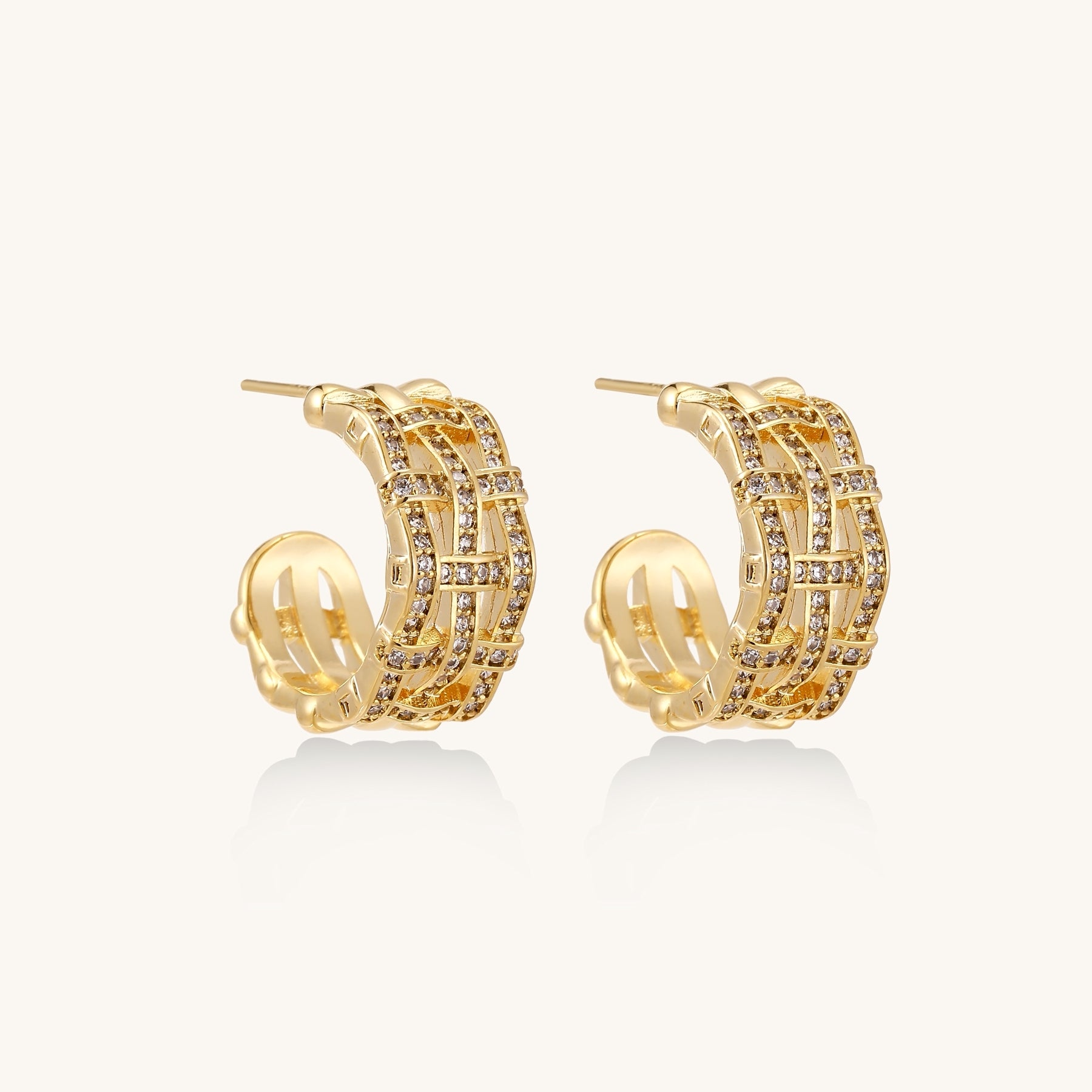 Close-up of geometric gold-plated hoop earrings with crystal pave in intricate lattice pattern on neutral background.