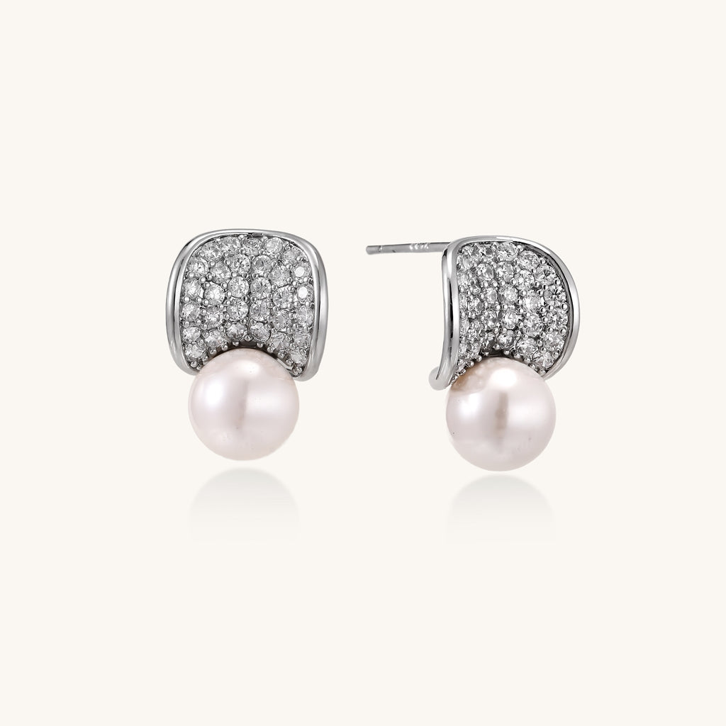 Elegant gold-plated curved earrings with diamond pavé crescents and suspended freshwater pearls on neutral background.