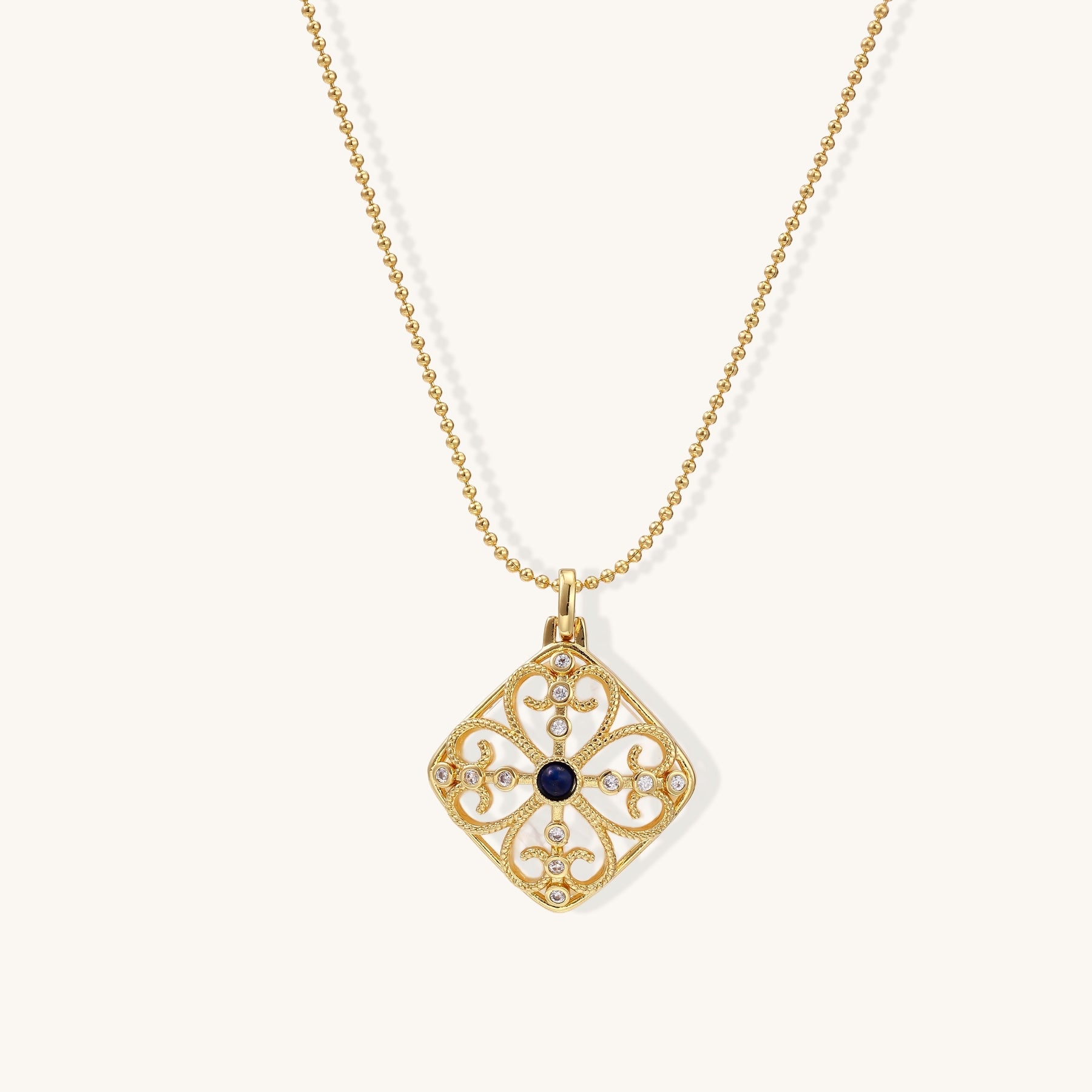 Gold-plated square pendant with ornate scrollwork featuring central blue lapis lazuli stone on ball chain